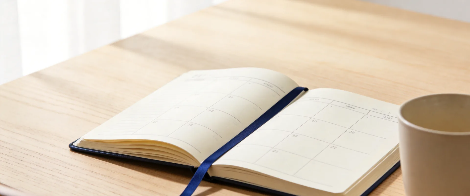 An open appointment diary with blank pages and a deep blue ribbon marker resting on a pale oak desk