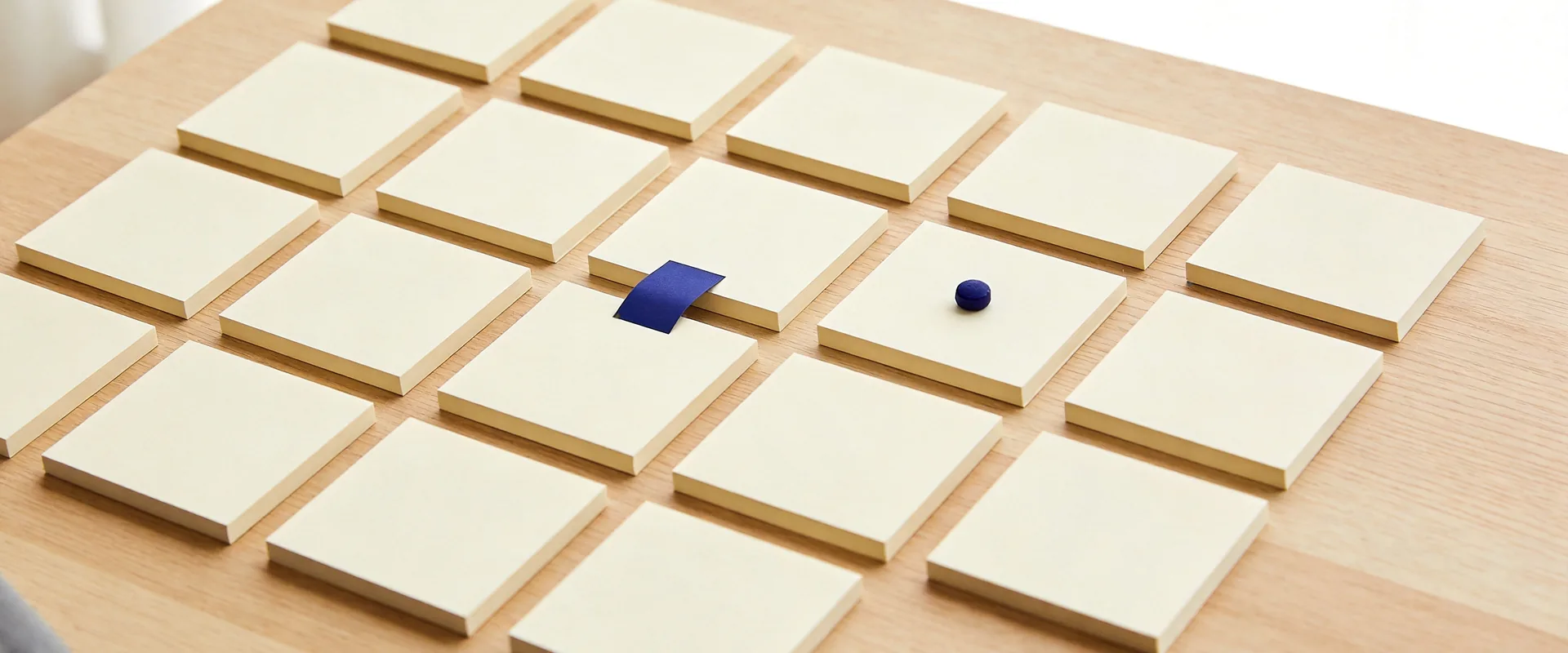 A tidy grid of blank cream note cards laid out on a pale oak desk, every one accounted for