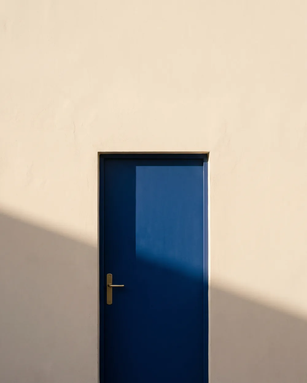 A deep cobalt blue front door set into a sunlit cream plaster wall